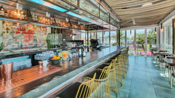Un espace bar moderne doté d’un long comptoir, de tabourets et d’une grande fenêtre offrant une vue sur l’extérieur.