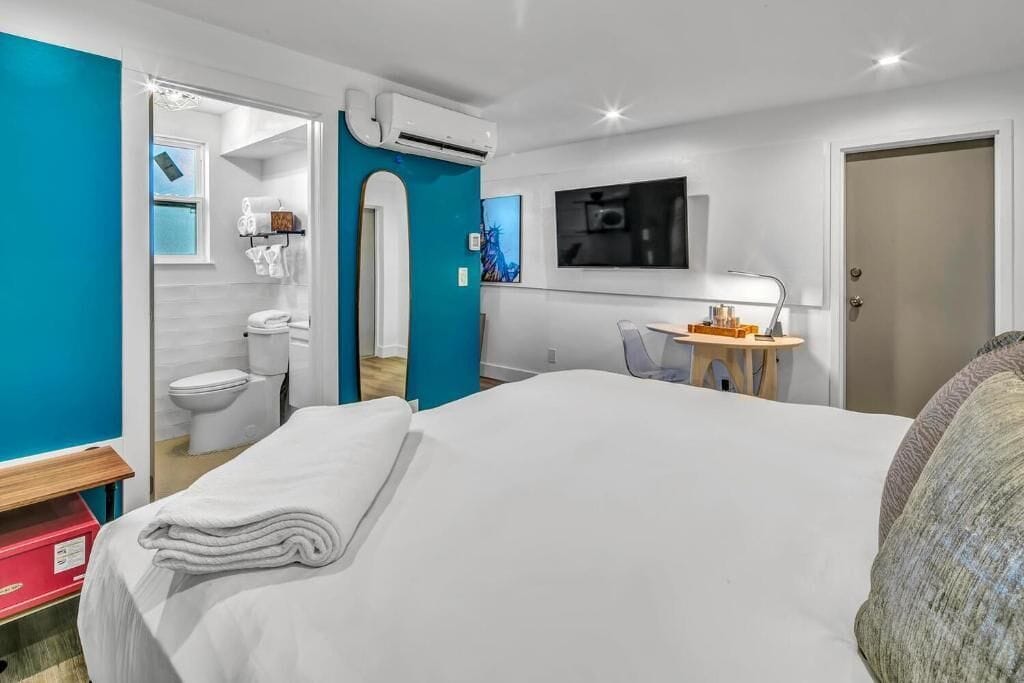 Camera d'albergo con un letto, una scrivania con una sedia, una televisione e un bagno visibile attraverso una porta aperta.