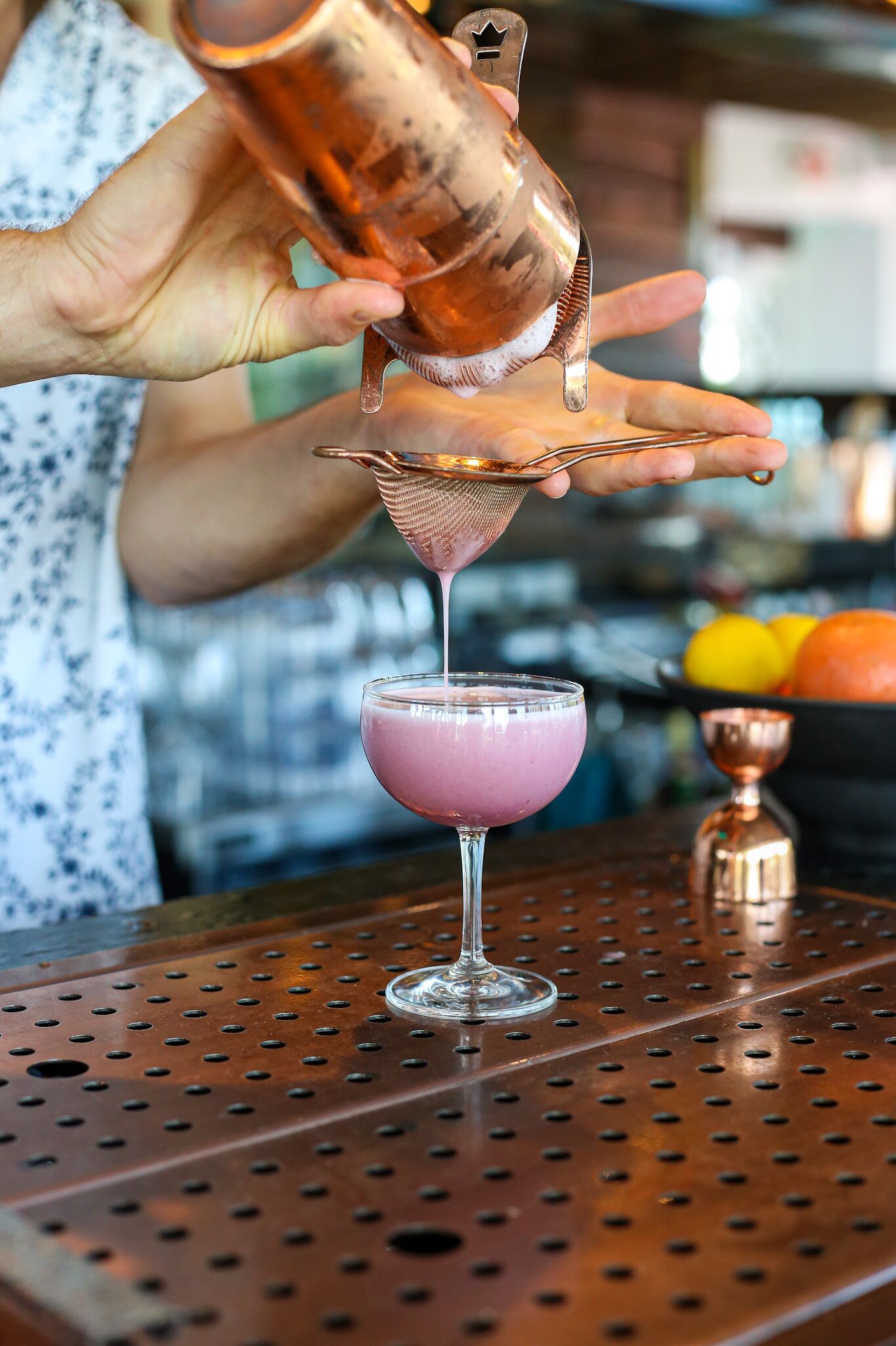 A bartender pouring a pink drink into a martini glass.
