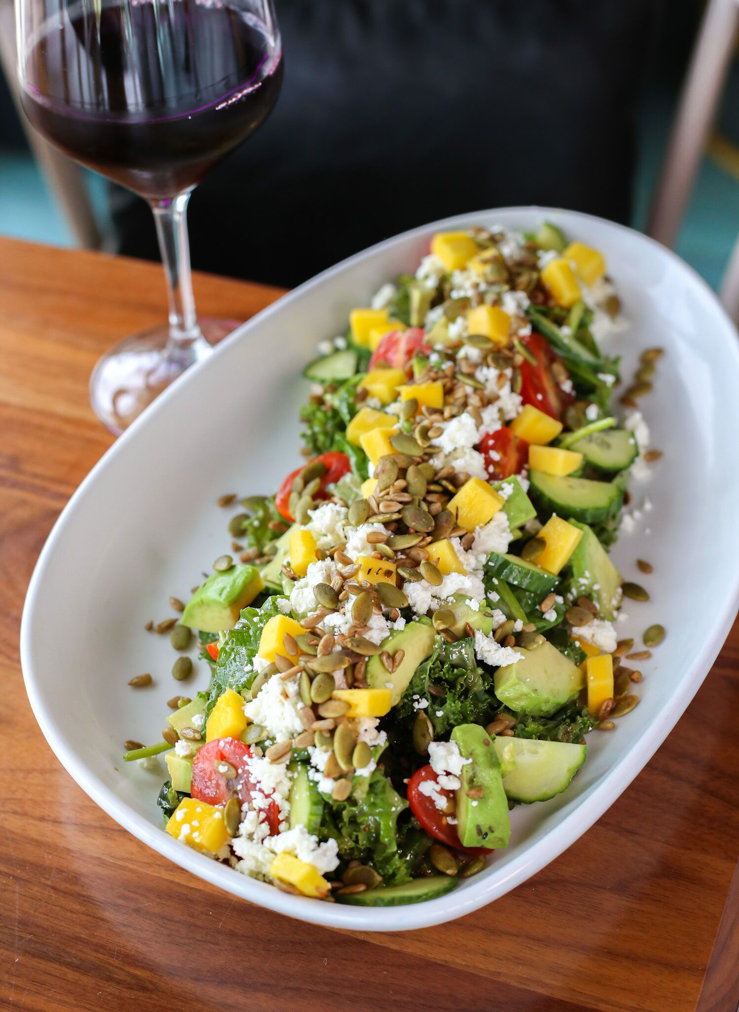 Une assiette ovale blanche sur laquelle est servie une salade colorée, le tout posé sur une table en bois.