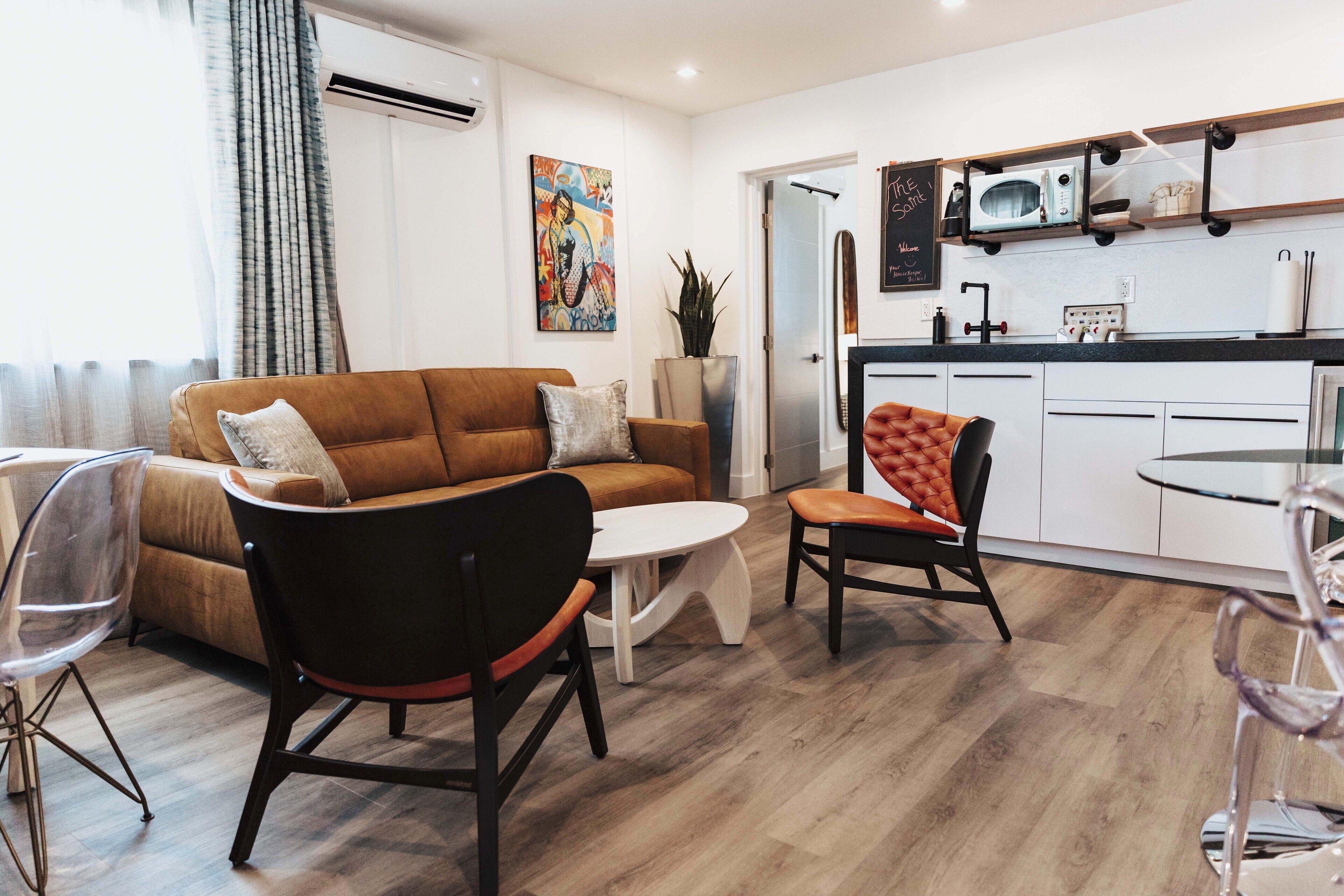 A modern living room with a brown sofa, a round white table, and a glass chair.