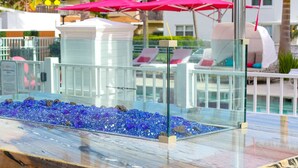 Un espace piscine agrémenté de parois en verre, de chaises longues et de parasols roses.