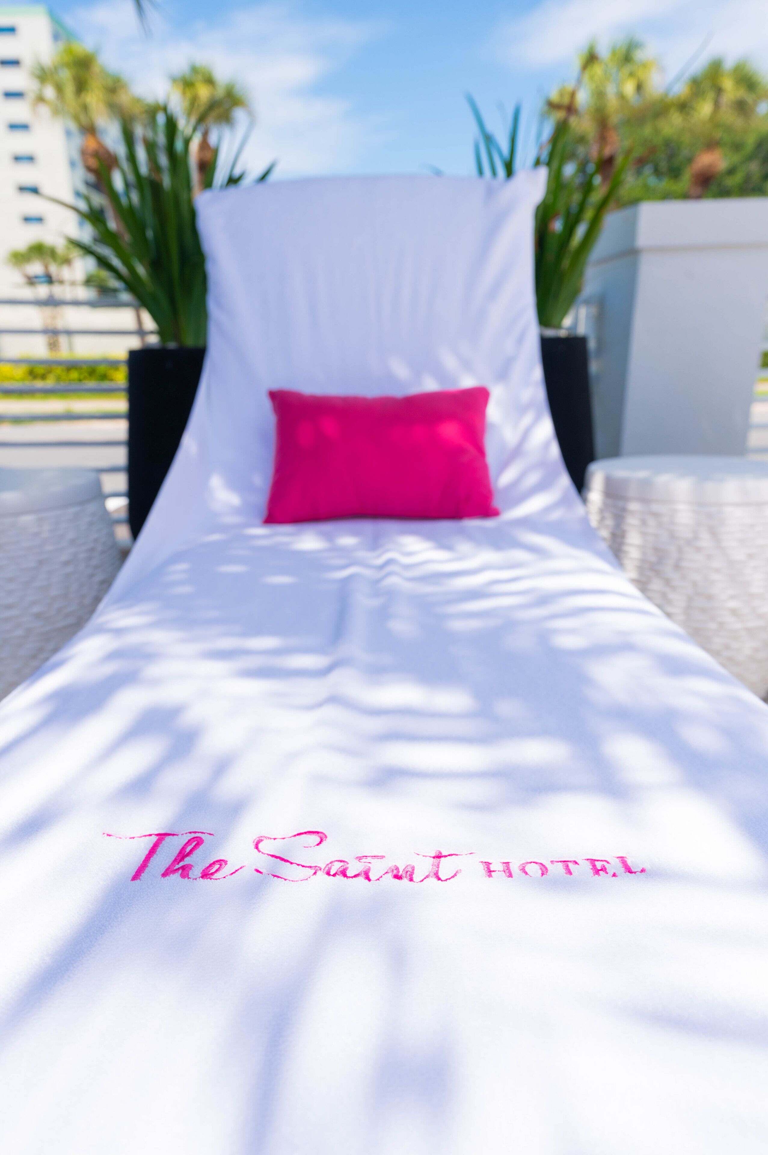 Una cama blanca con un almohadón rosa y el texto "The Saint Hotel" sobre una superficie blanca.