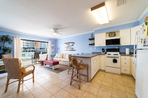 A kitchen with a dining area, featuring a large island, white cabinets, and a view of a balcony.