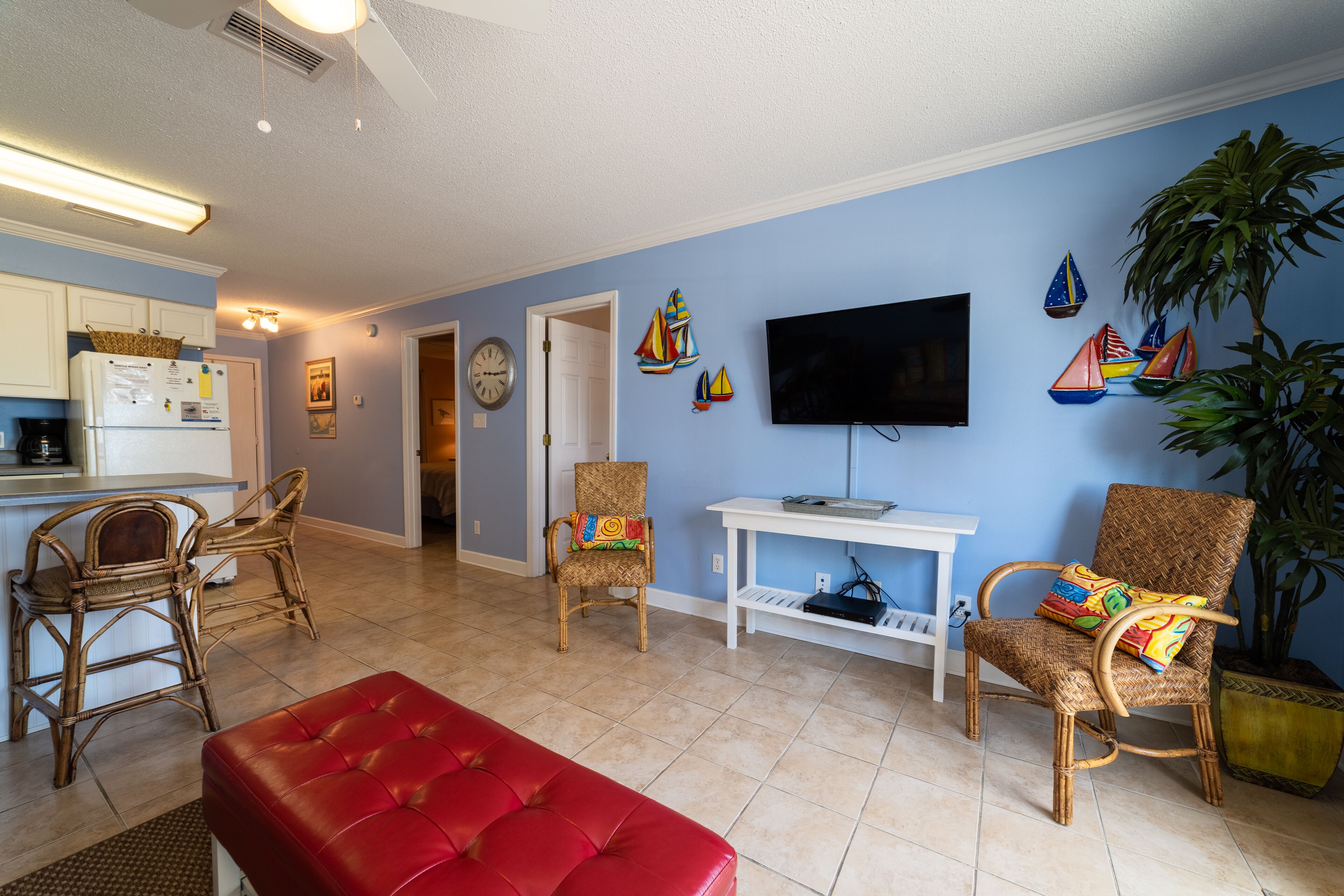 A living room with a red sofa, wicker chairs, a television, and a potted plant.