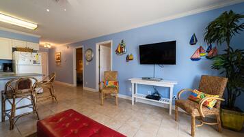 A living room with a red sofa, wicker chairs, a television, and a potted plant.