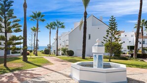 A white building with a fountain, surrounded by palm trees and a clear sky.