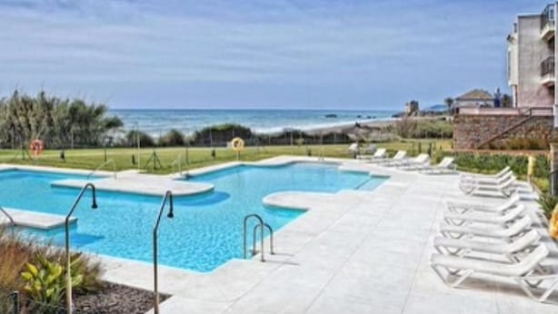 A swimming pool with a view of the ocean, surrounded by lounge chairs and a building.