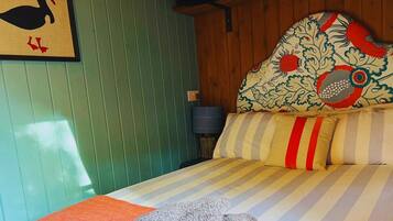 A room with a bed, a headboard with a floral pattern, and a wall with a framed picture of a duck.