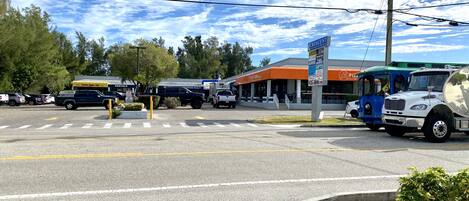A parking lot with various vehicles, a gas station, and a building with multiple businesses including a pizza place.