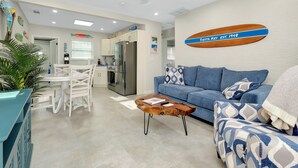 A modern living room with a blue sofa, a coffee table, and a dining area with white chairs and a table. - Newly Remodeled-150 Yards to Beach and Restaurants! (Sarasota)
