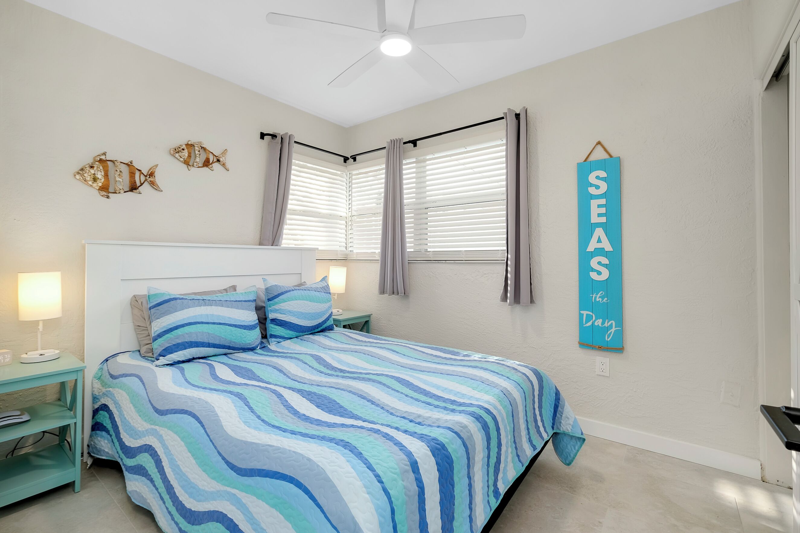 Une chambre à coucher comprenant un lit, des tables de chevet, un ventilateur de plafond et un panneau fixé au mur.