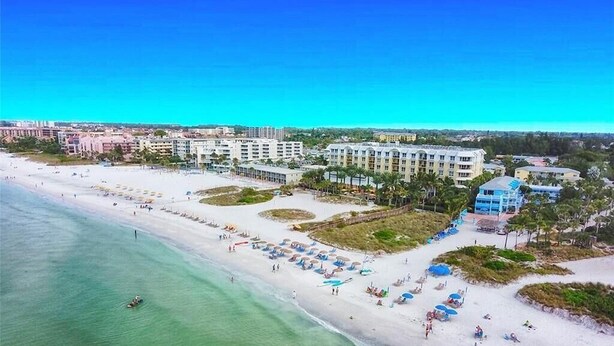 An aerial view of a beach resort with multiple hotel buildings, a sandy beach, and clear turquoise water. - Newly Remodeled-150 Yards to Beach and Restaurants! (Sarasota)