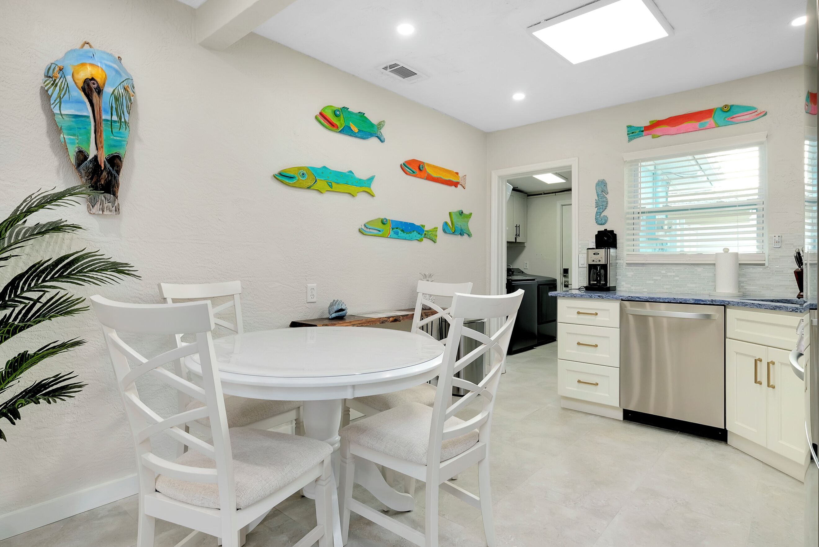 A kitchen with white cabinets, a dishwasher, and a dining area with white chairs and a round table.