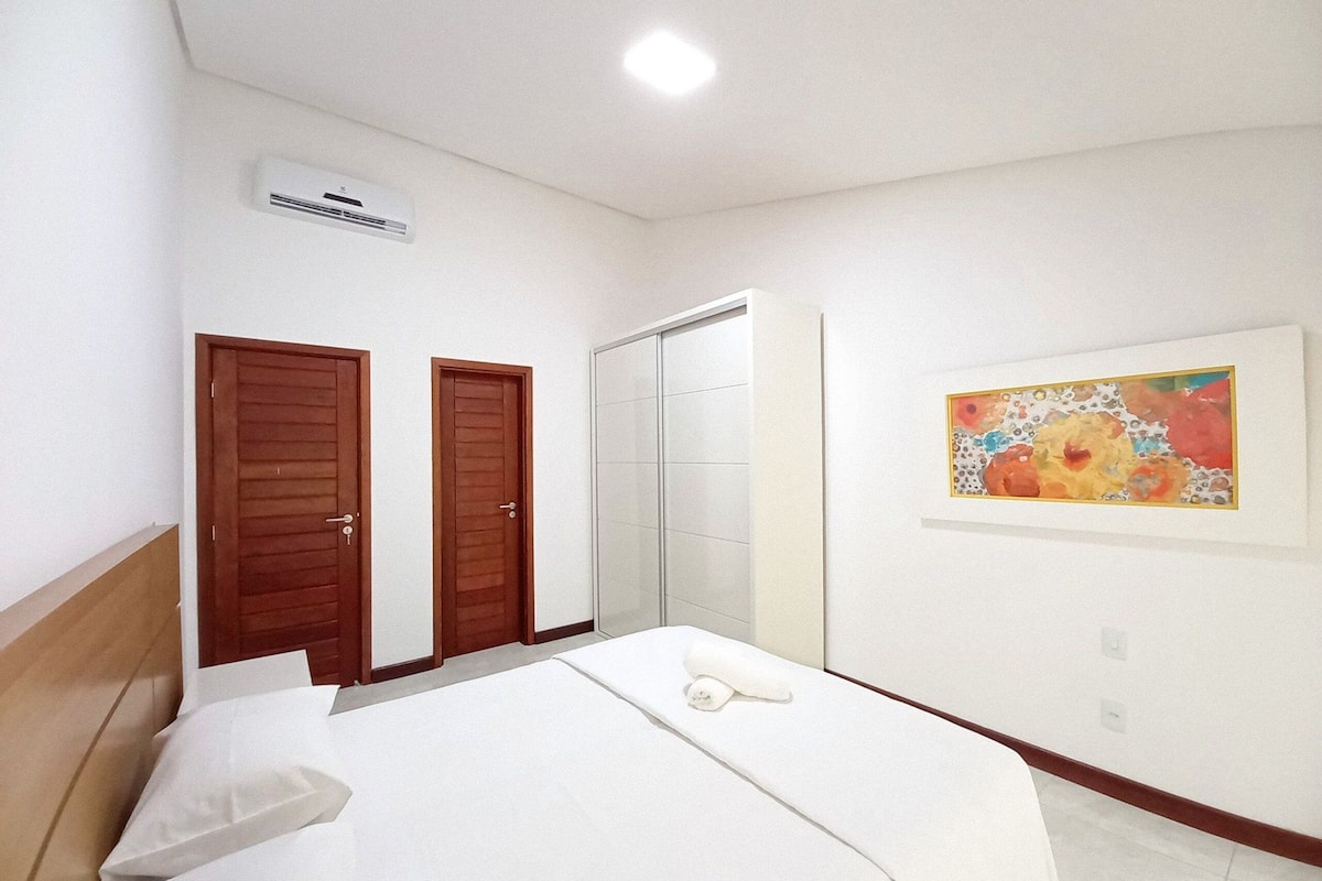 A bedroom with two wooden doors, a sliding glass door closet, a bed with white linens, and a colorful abstract painting on the wall.