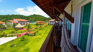 A balcony with a view of a well-maintained lawn, multiple buildings with red roofs, and a mountainous backdrop. - Flats at Club Meridional - Praia dos Carneiros (Tamandaré)