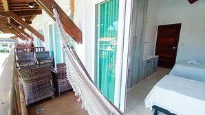Une chambre avec un lit, un hamac, des meubles en osier, une porte-fenêtre coulissante et une petite kitchenette.
