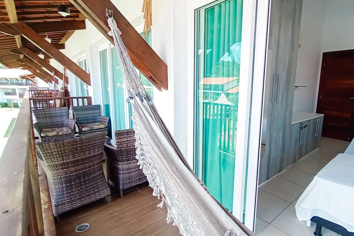 A room with a bed, a hammock, wicker furniture, a sliding glass door, and a small kitchenette.