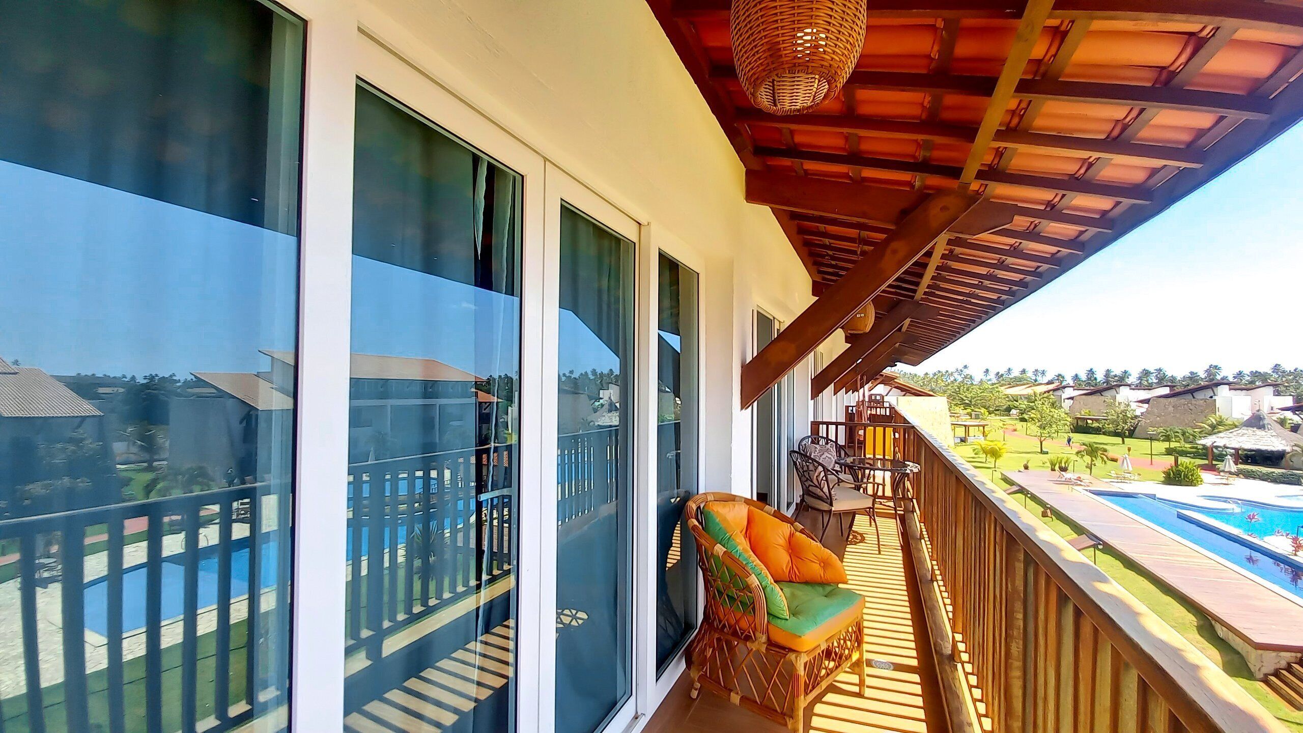 A balcony with a view of a swimming pool, a wicker chair, and a wooden deck.