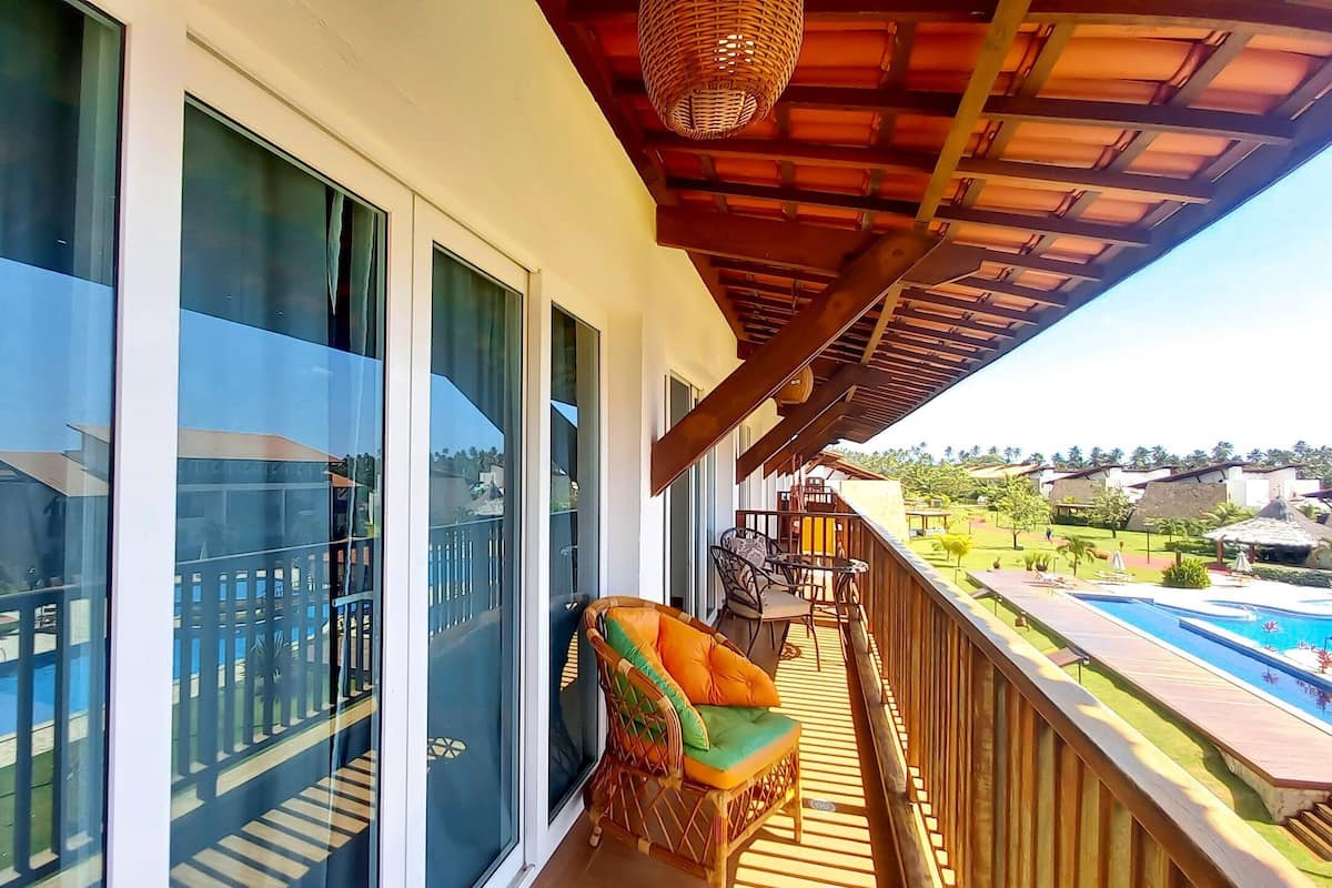 A balcony with a view of a swimming pool, a wicker chair, and a wooden deck.