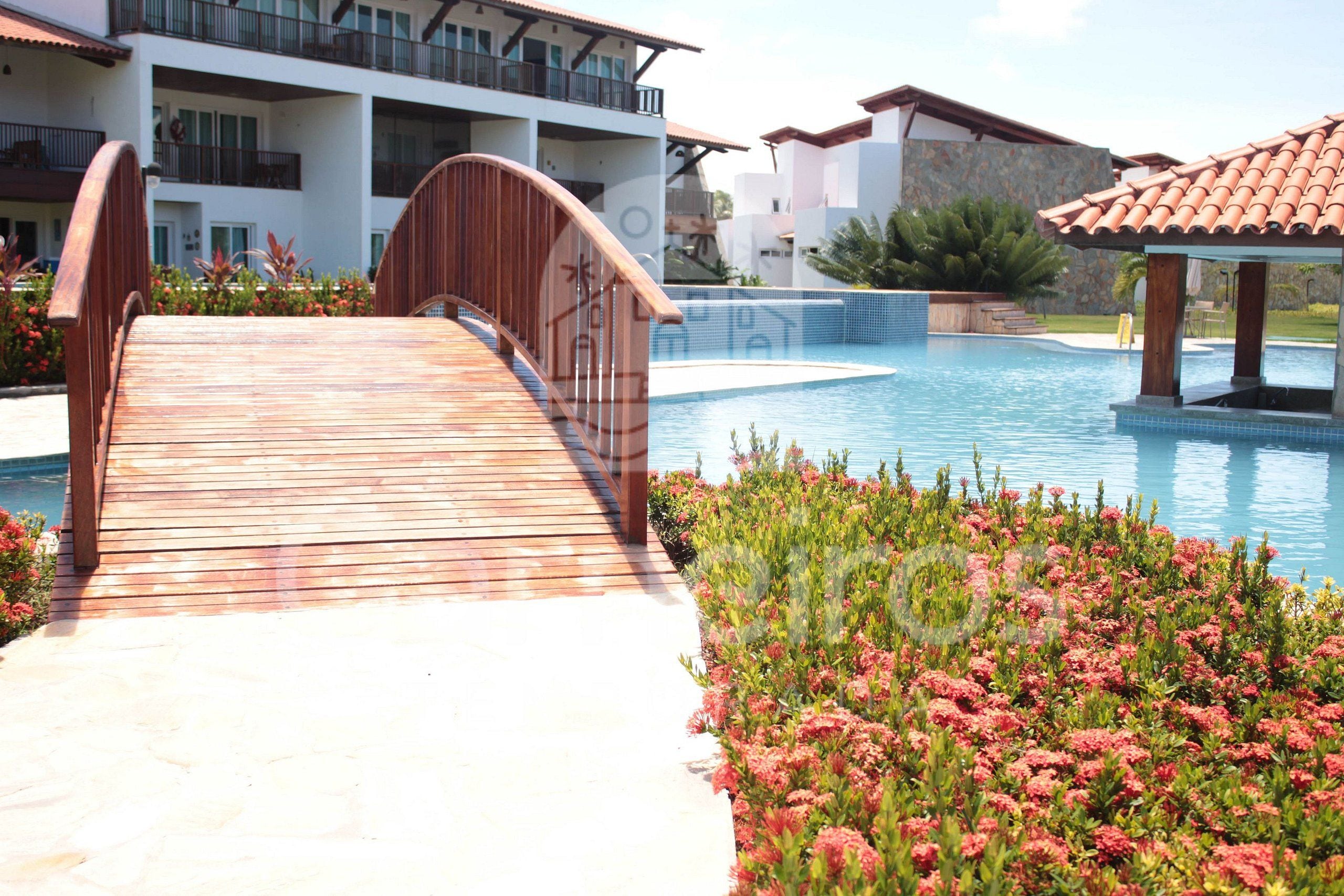 A wooden bridge leading to a swimming pool with a view of a multi-story building in the background.