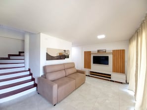 Un salon moderne avec un canapé, un téléviseur à écran plat et un escalier.