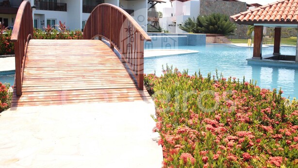 Un pont en bois mène à une piscine, et on aperçoit, en arrière-plan, un immeuble à plusieurs étages.