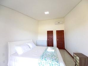 Ein Schlafzimmer mit einem Bett, einem Schminktisch, zwei Türen und einer Klimaanlage.