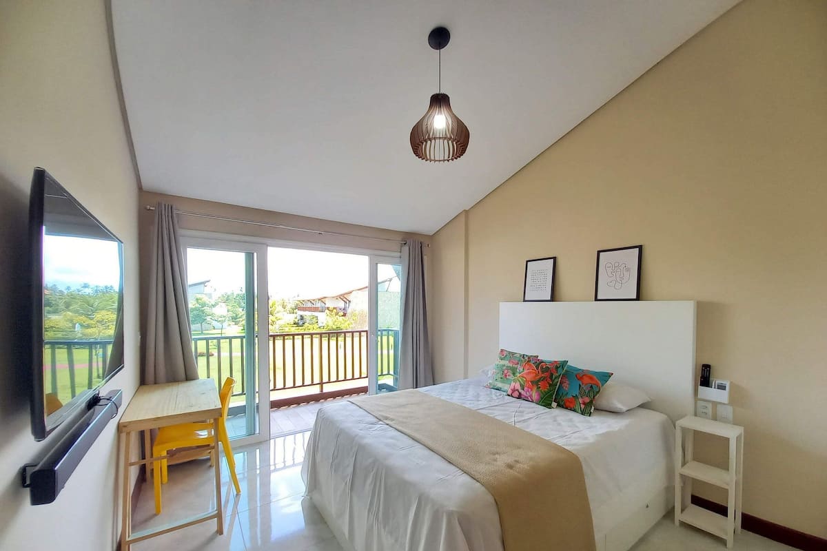 A hotel room with a bed, a desk, a chair, a TV, a balcony with a view, and a ceiling light.