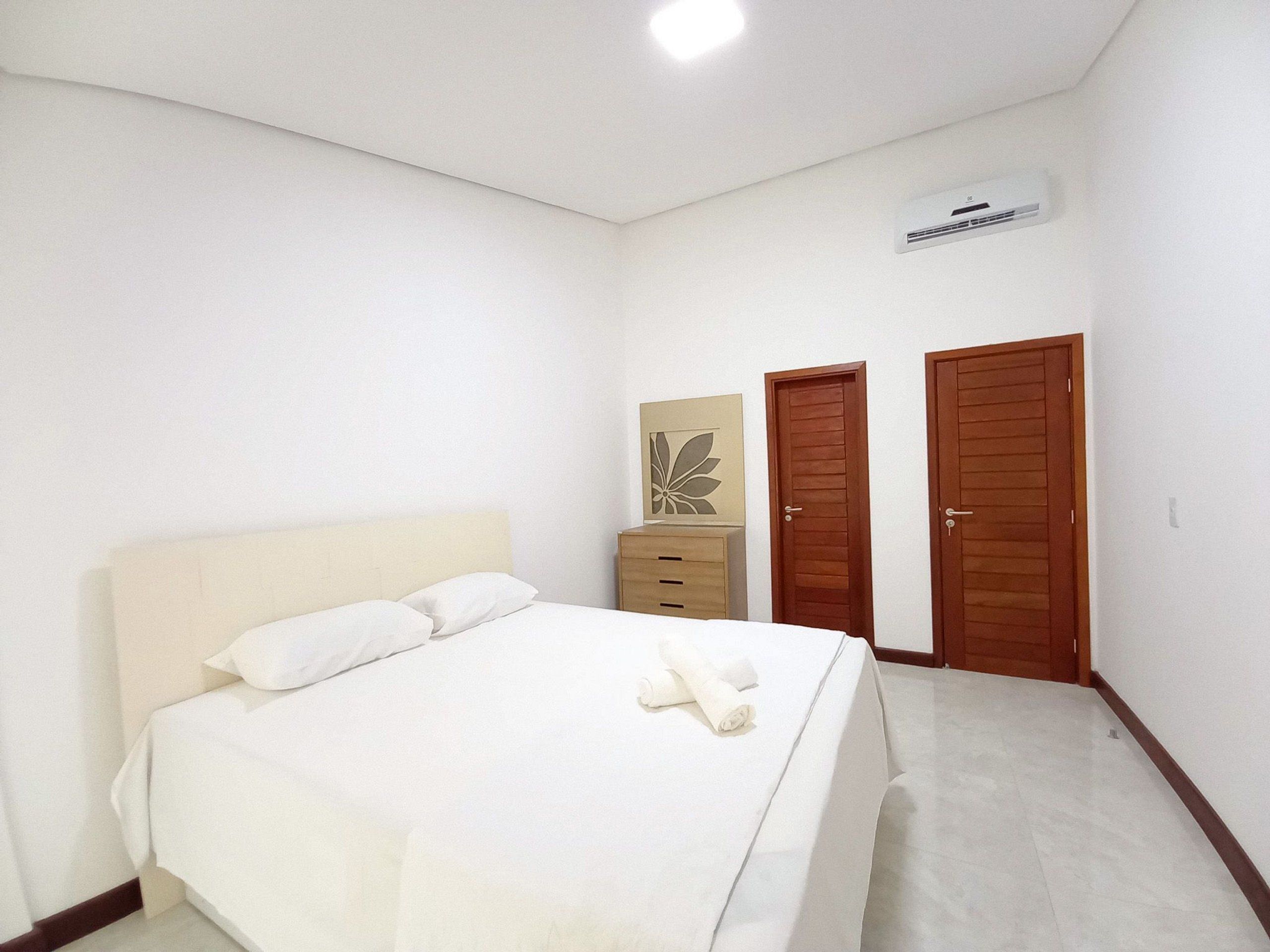 Een slaapkamer met een bed, een dressoir, twee deuren en een airconditioning.