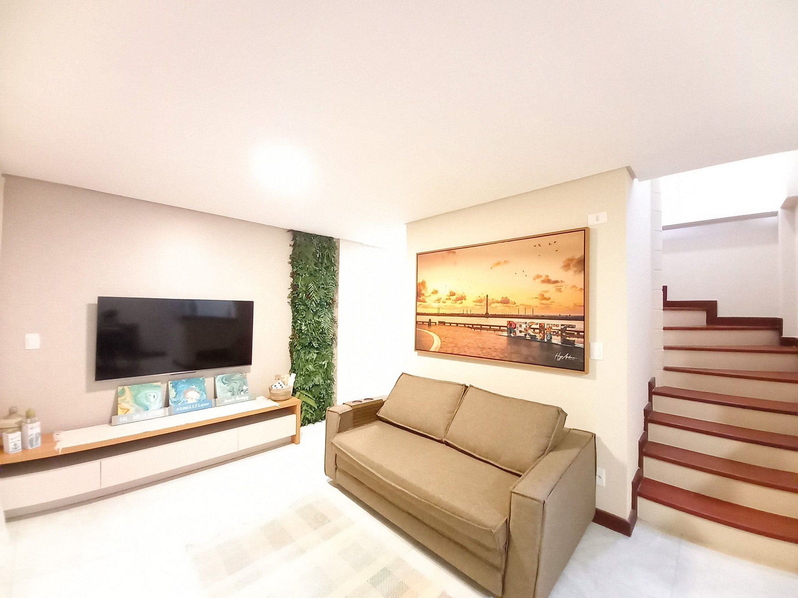 A living room with a flat-screen TV, a sofa, a painting, and a staircase.