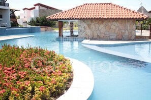 Piscina com estrutura de pedra, rodeada por um canteiro de flores e um edifício com telhado em azulejos.