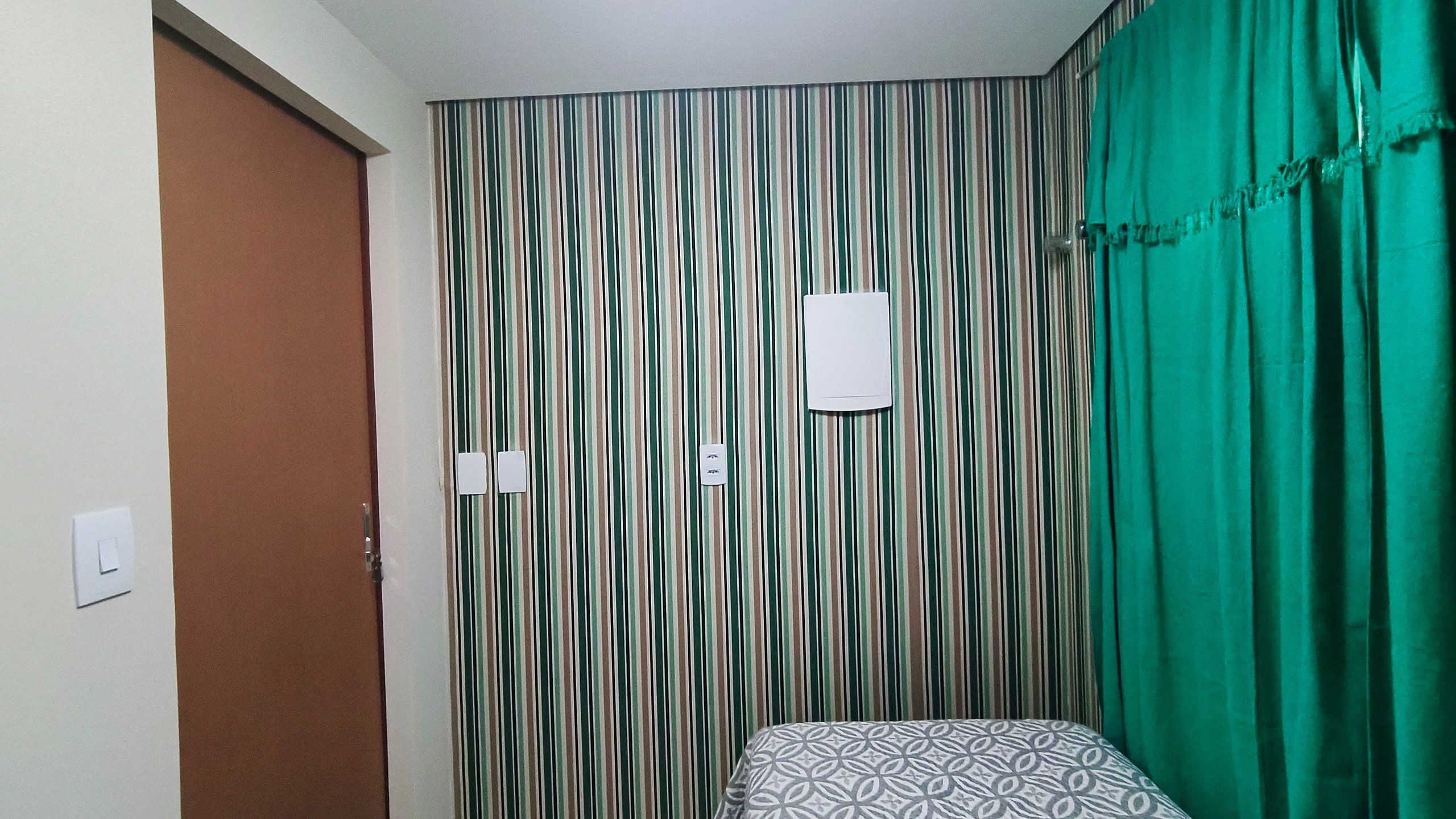 A room with a striped wall, a bed with a patterned bedspread, a green curtain, and a whiteboard on the wall.