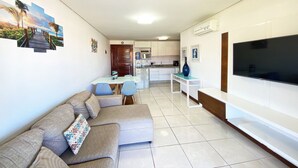Un salon comprenant un canapé, un téléviseur et un coin repas avec une table et des chaises.