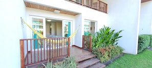 A two-story building with a wooden deck, a hammock, and a small garden with plants and flowers. - Flats at Club Meridional - Praia dos Carneiros (Tamandaré)