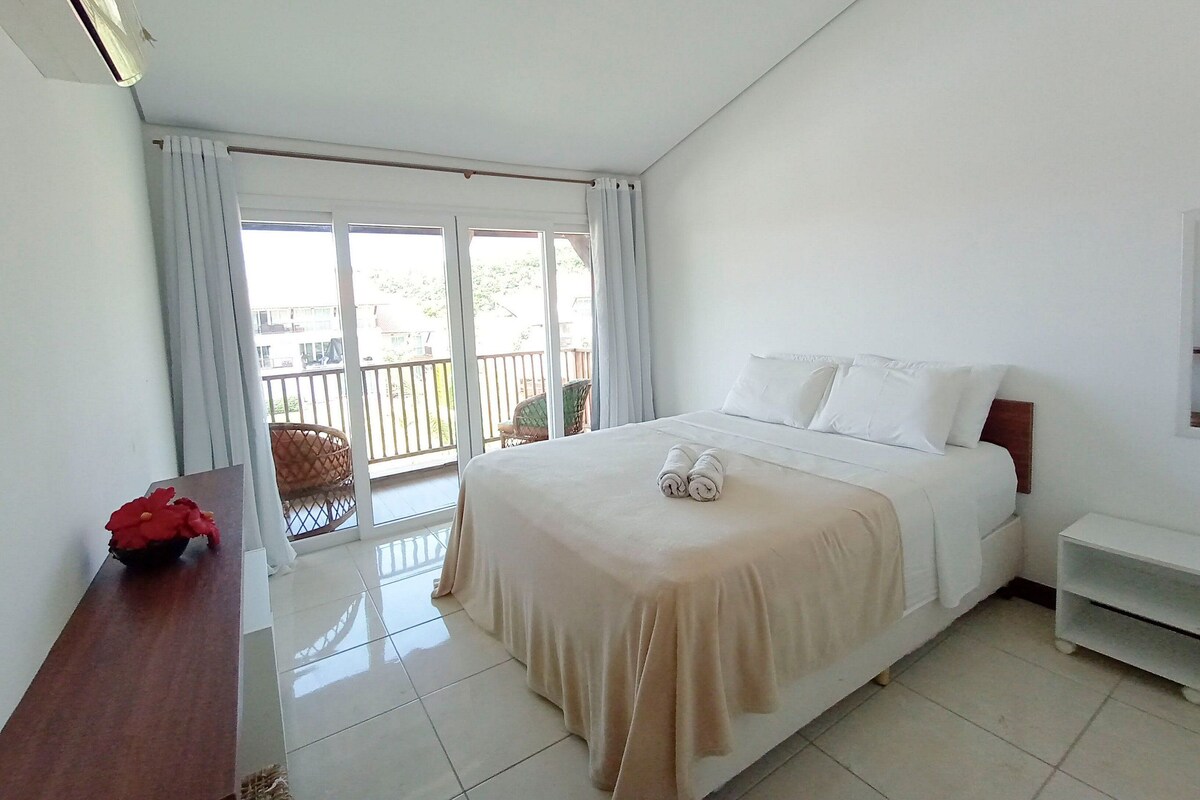 A hotel room with a bed, a desk, a chair, and a balcony with a railing.