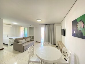 Quarto de hotel com cama, sofá, mesa de jantar com cadeiras, televisão e um quadro na parede.