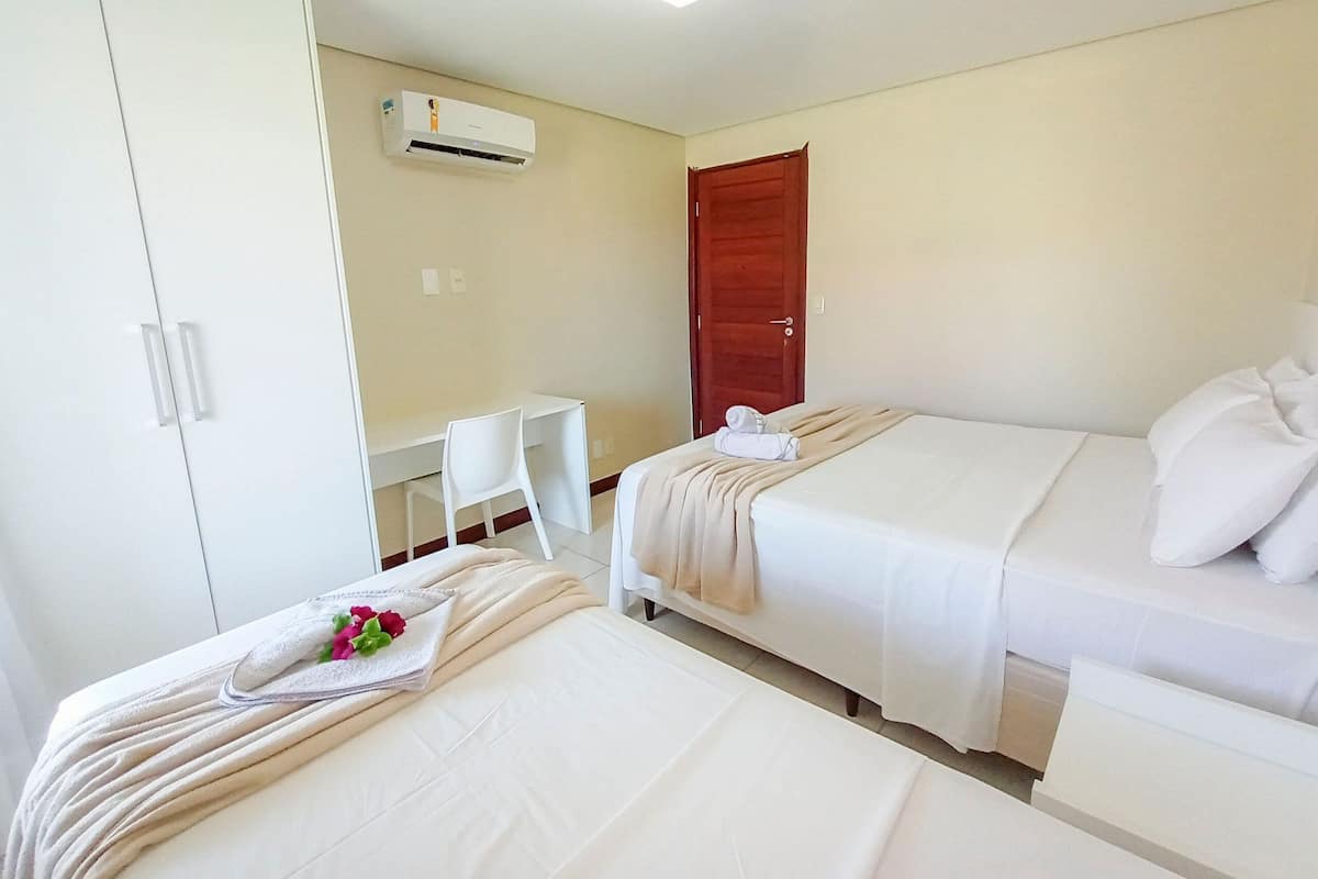 A hotel room with two beds, a desk, a chair, an air conditioning unit, and a wooden door.