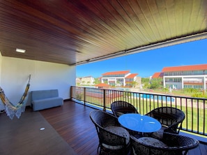 A covered outdoor area with a hammock, a sofa, and wicker chairs around a glass table.