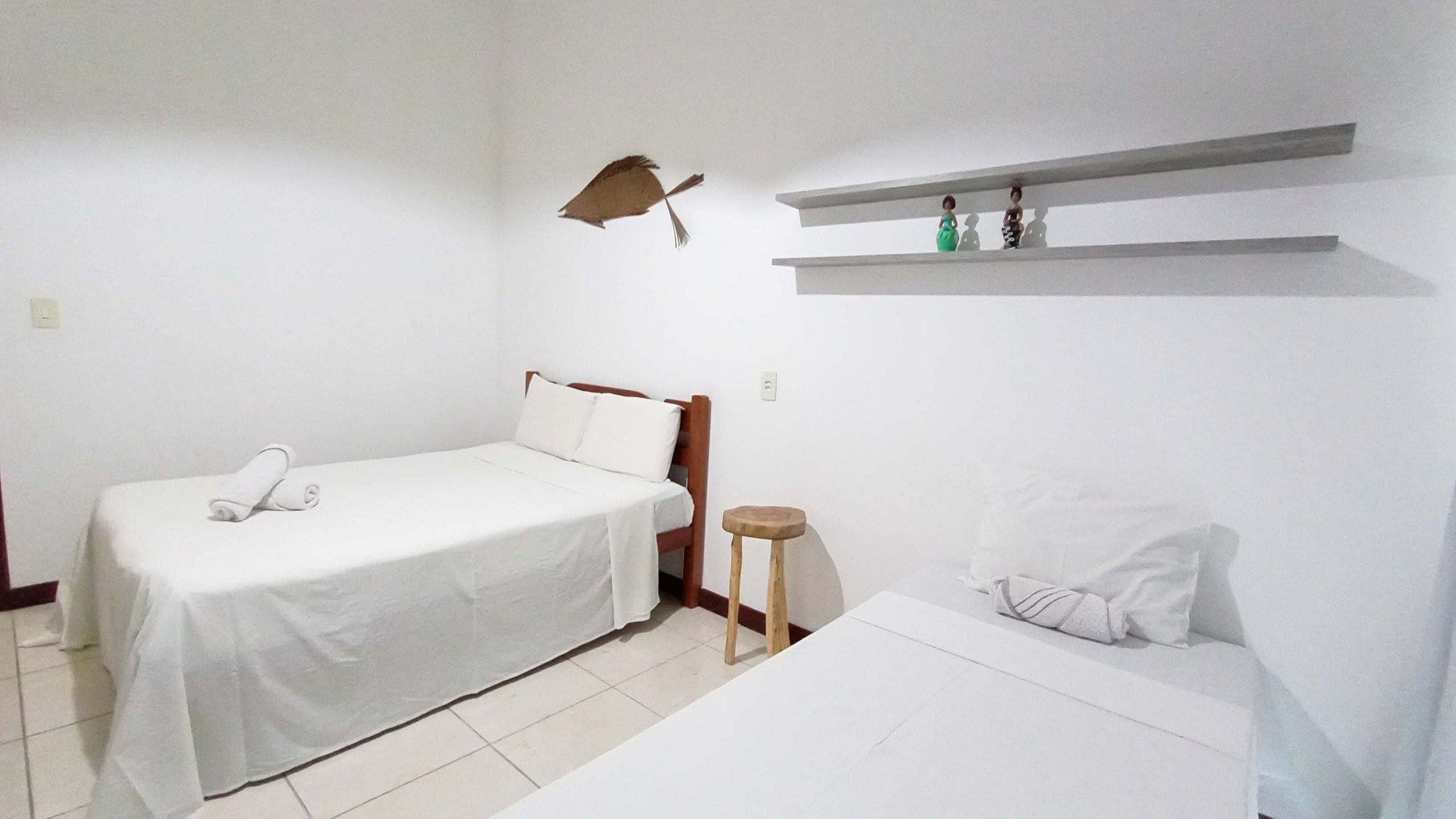 A simple, clean room with a bed, a small stool, and a shelf with decorative items.