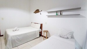 A simple, clean room with a bed, a small stool, and a shelf with decorative items.