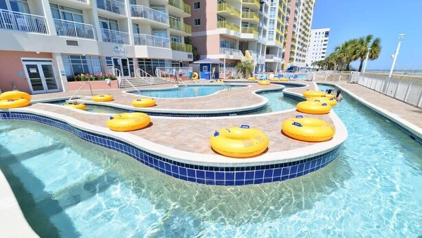 A pool area with multiple lanes and yellow floating rings, surrounded by a multi-story building with balconies. - North Myrtle Beach Oceanfront Condo w Lazy River (North Myrtle Beach)
