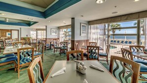 A hotel dining area with tables and chairs, large windows with a view of the ocean, and a green carpeted floor. - North Myrtle Beach Oceanfront Condo w Lazy River (North Myrtle Beach)