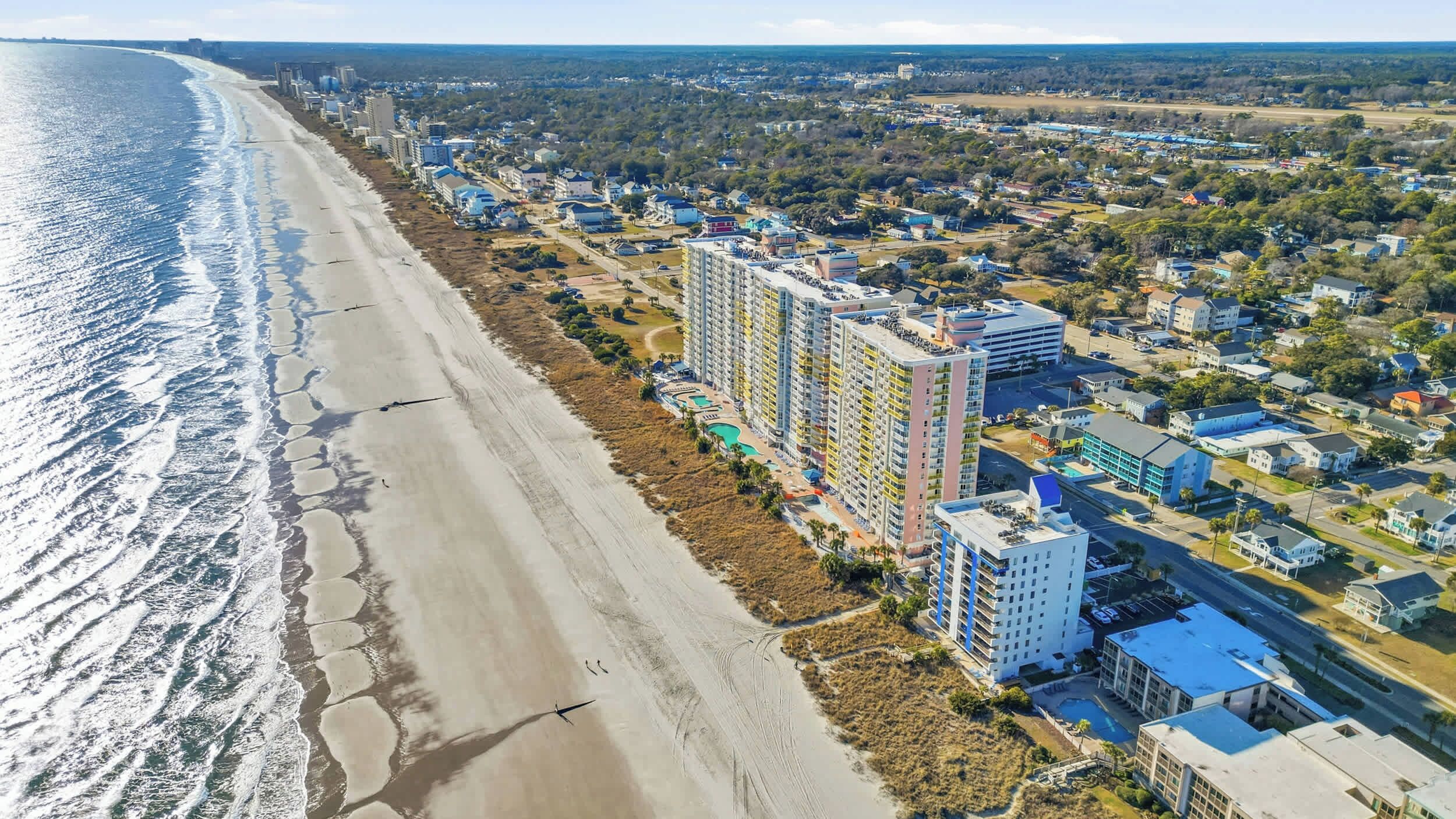 Un paysage urbain côtier avec un hôtel en bord de mer, comprenant plusieurs immeubles de grande hauteur, une piscine et une plage.