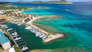 An aerial view of a marina with boats docked, a beach, and a coastal town with buildings.