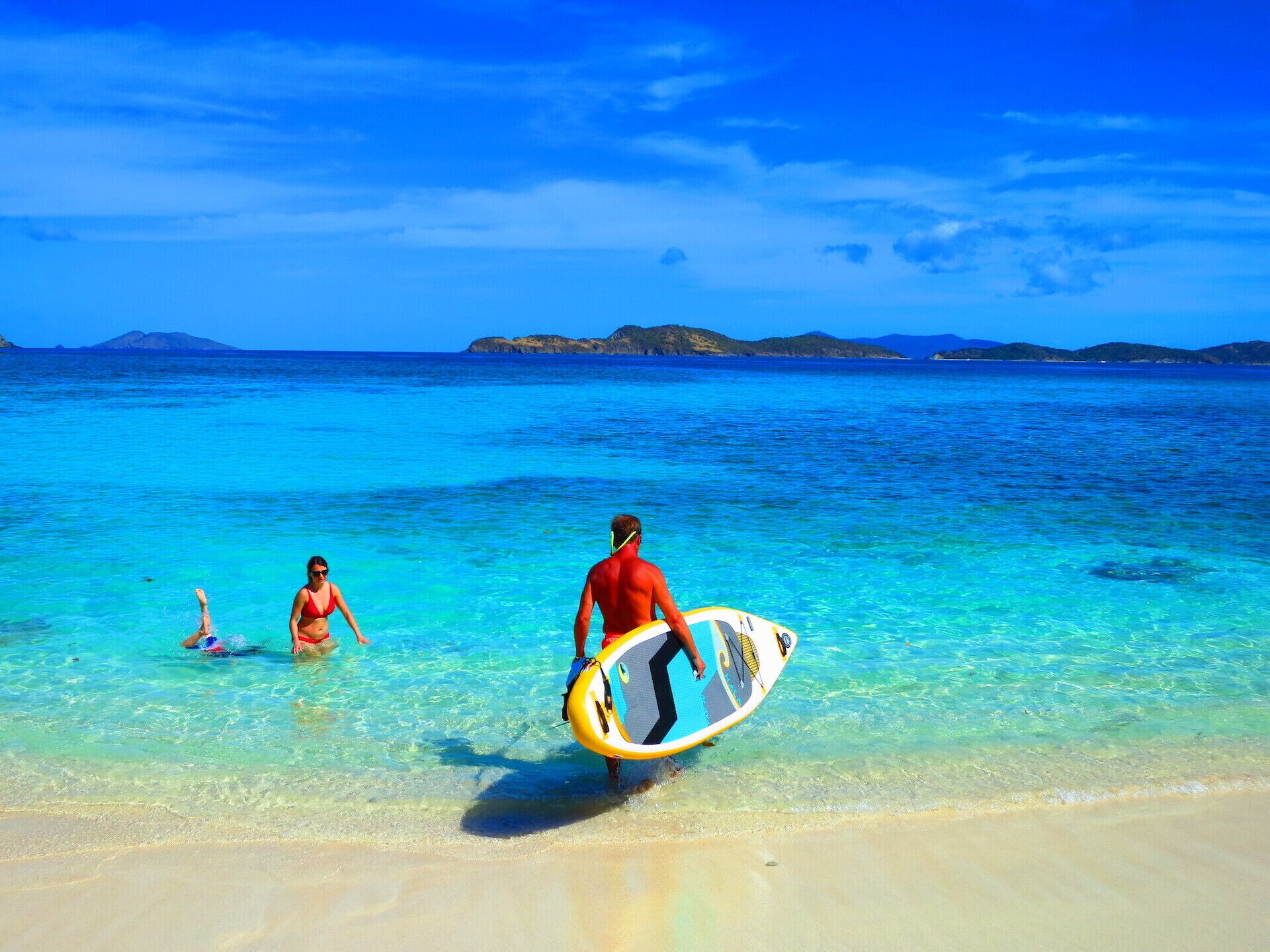 A beach with clear turquoise water and distant islands.
