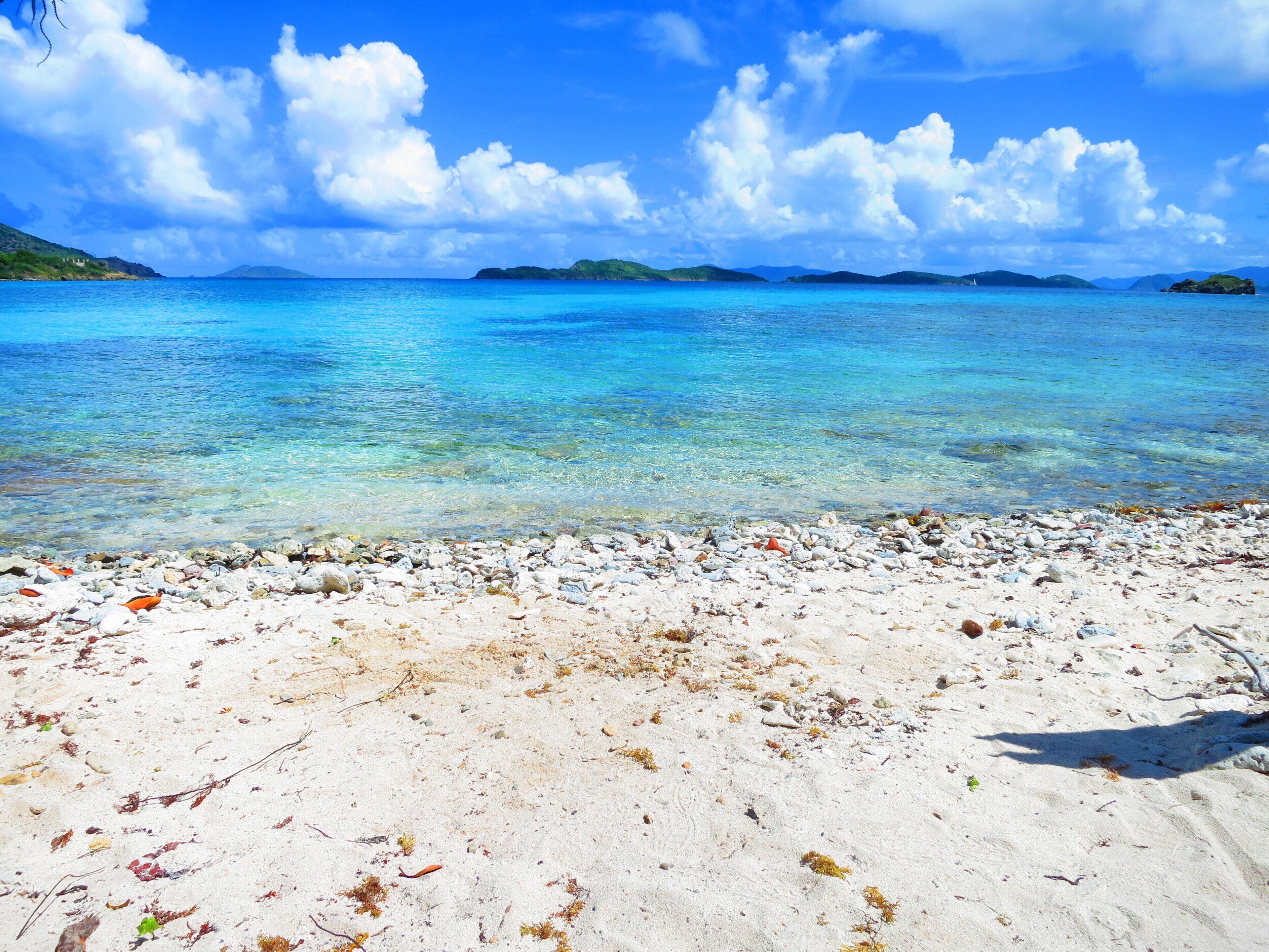 A beach with clear turquoise water, white sand, and scattered rocks.