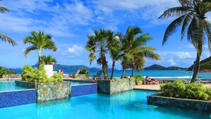 A pool area with clear blue water, surrounded by palm trees and a view of the ocean.