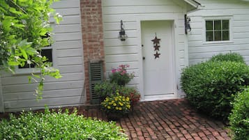 A white house with a brick chimney, a white door with star decorations, and a brick pathway.