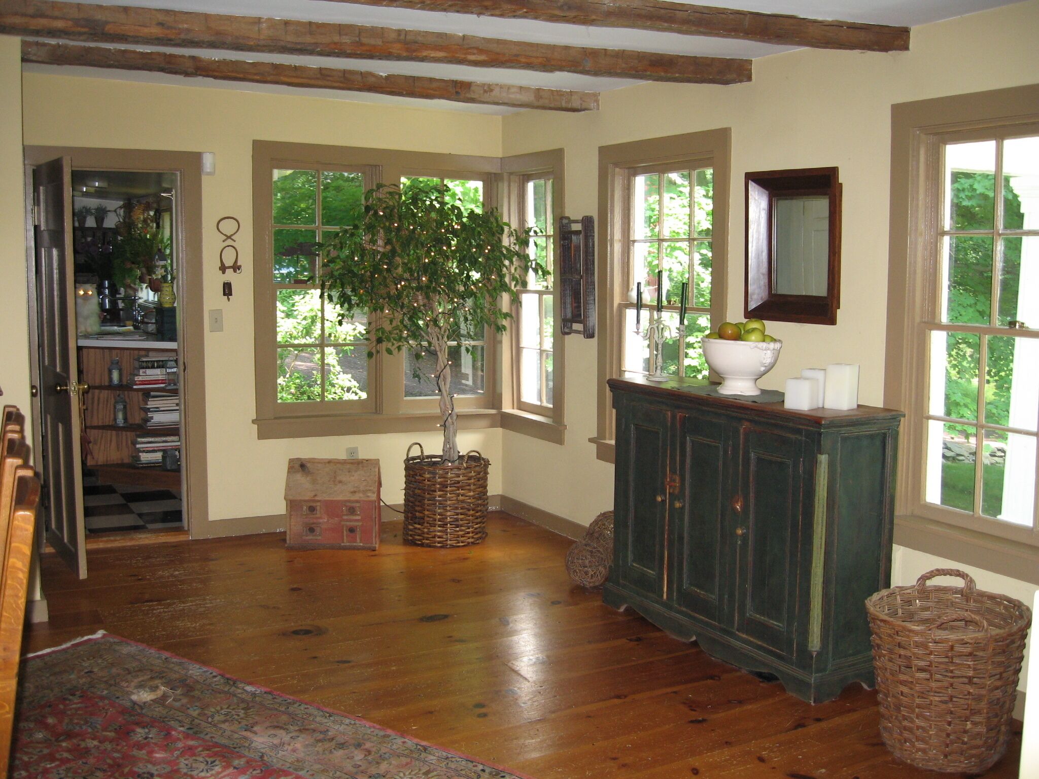 A spacious room with wooden flooring, a large window, a cabinet, and a small table with a bowl of fruit.